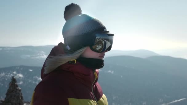 Retrato de uma menina bonita olhando para a montanha. Um turista em uma máscara ou óculos de snowboard olha para a frente. O conceito de vitória no desporto. Viagem de inverno na estância de esqui — Vídeo de Stock