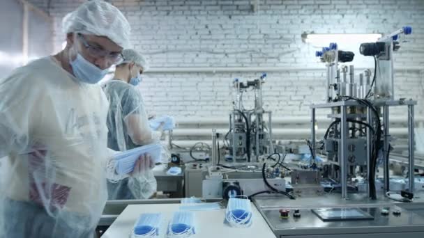 Koruyucu tıbbi maskeler üreten bir fabrikadan bir grup işçi. Yüz maskeleri plastik torbalara konur. Coronavirüs veya covid-19 'a karşı koruyucu ekipman üretmek için makine — Stok video