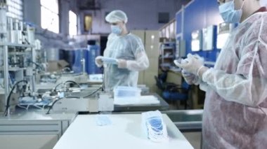 Koruyucu tıbbi maskeler üreten bir fabrikadan bir grup işçi. Yüz maskeleri plastik torbalara konur. Coronavirüs veya covid-19 'a karşı koruyucu ekipman üretmek için makine