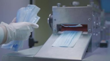 Tıbbi koruyucu yüz maskeleri üretimi. Coronavirus koruma makinesi, covid-19. Bitmiş maskeler makineden çıkıyor. İşçi maskeleri bir çantada topluyor.