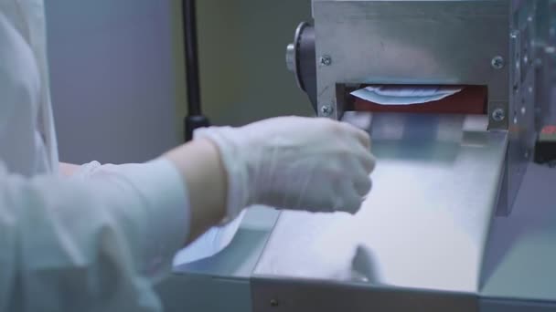 Production of medical protective face masks. Coronavirus protection machine, covid-19. The finished masks come out of the machine. The worker collects the masks in a pack — Stock Video