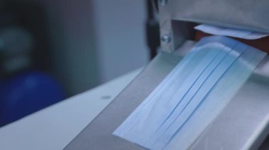 Tıbbi koruyucu yüz maskeleri üretimi. Coronavirus koruma makinesi, covid-19. Bitmiş maskeler makineden çıkıyor. İşçi maskeleri bir çantada topluyor..