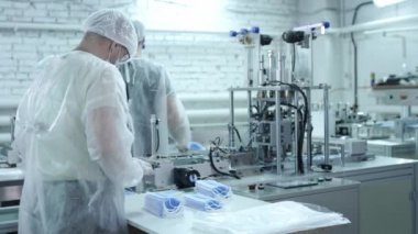 Koruyucu tıbbi maskeler üreten bir fabrikadan bir grup işçi. Yüz maskeleri plastik torbalara konur. Coronavirüs veya covid-19 'a karşı koruyucu ekipman üretmek için makine