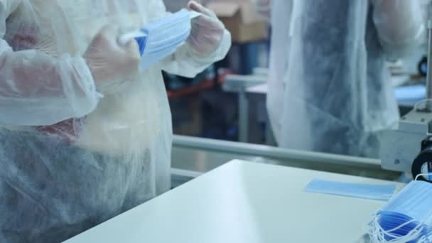 Un groupe de travailleurs d'une usine pour la production de masques médicaux de protection. Les masques sont emballés dans des sacs en plastique. Machine pour créer des équipements de protection contre le coronavirus ou le covide-19 — Video