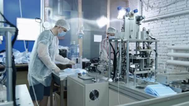 A group of workers from a factory for the production of protective medical masks. Face masks are packed in plastic bags. Machine for creating protective equipment against coronavirus or covid-19 — Stock Video