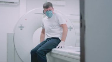 Tıbbi maskeli bir hasta modern bir tomografi makinesinin önünde yatıyor. Doktor tomografide akciğerleri analiz ediyor. Covid ya da Coronavirus tehlikesi. Akciğerlerin organı inceleniyor..