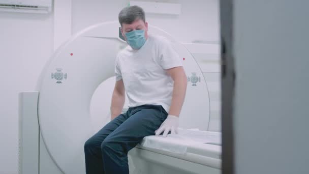 Ein Patient mit medizinischer Maske liegt an einem modernen Computertomographen-Gerät. Der Arzt analysiert die Lunge mit einem CT-Gerät. Die Gefahr von Covidien oder Coronaviren. Untersuchung des Lungenorgans. — Stockvideo