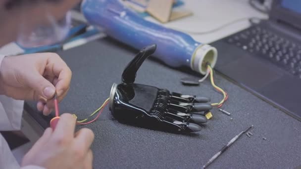 Инженер-учёный создает или диагностирует роботизированный протез руки. Протезная лаборатория, промышленное производство. Механическая рука для полноценной жизни. Создание кибернетических конечностей. — стоковое видео
