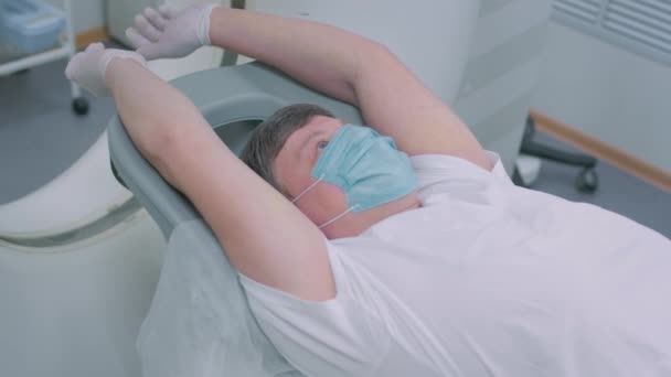 의료용 마스크를 쓴 환자는 현대 컴퓨터 단층 촬영 기계에 누워 있습니다. 의사는 CT 스캐너로 폐를 분석 합니다. 코로나 바이러스나 코로나 바이러스의 위험성. 폐의 기관을 조사 함. — 비디오