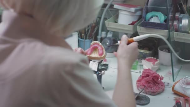 Médico femenino adulto crea una mandíbula dentaria en el laboratorio. Cirujano sosteniendo una prótesis dental. Tecnología avanzada en odontología. Producción de implantes dentales y dientes artificiales. EPIC ROJO. — Vídeo de stock