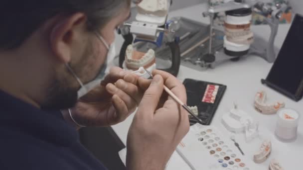 A dentist creates a model of a jaw prosthesis and ceramic teeth in the laboratory. Apply paint to dental implants with a brush. Artificial teeth. Application of new technologies in dentistry — Stock Video