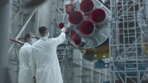 Dois engenheiros cientistas inspeccionam a nave espacial, escrevem no tablet. Um foguete espacial num hangar militar a ser preparado para o lançamento. Tecnologias espaciais. Construção de Big Rocket. A Humanidade no Espaço. — Vídeo de Stock