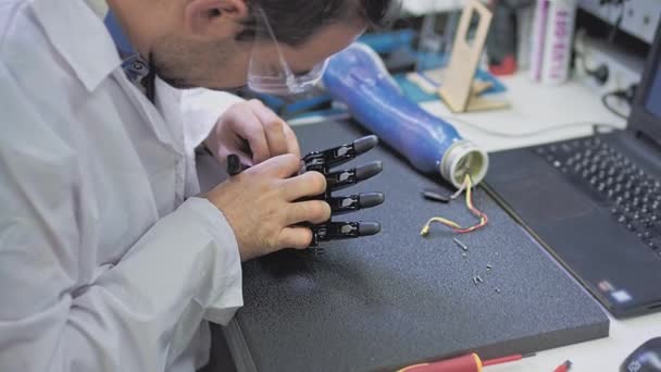 Producción de una mano protésica. Un ingeniero científico crea o diagnostica una prótesis de brazo robótico. Laboratorio protésico. Un brazo mecánico para una vida plena. Creación de extremidades cibernéticas — Vídeos de Stock