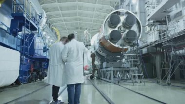 İki mühendis uzay gemisini inceliyor, tablete yazıyor. Askeri bir hangarda fırlatılmaya hazır bir uzay roketi. Uzay teknolojileri. Big Rocket 'in inşaatı. Uzayda İnsanlık.