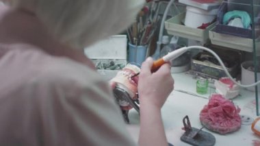 Yetişkin kadın sıhhiyeci laboratuarda takma diş yapıyor. Diş protezi tutan bir cerrah. Dişçilikte gelişmiş teknoloji. Diş implantı ve yapay diş üretimi. Kırmızı EPIC.