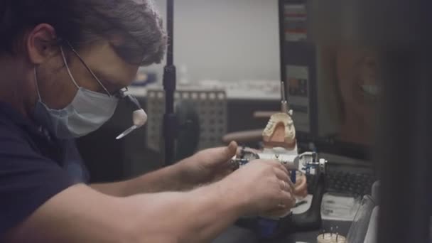 Un dentista crea un modelo de prótesis de mandíbula y dientes de cerámica en el laboratorio. Aplique pintura a los implantes dentales con un pincel. Dientes artificiales. Aplicación de nuevas tecnologías en odontología — Vídeos de Stock