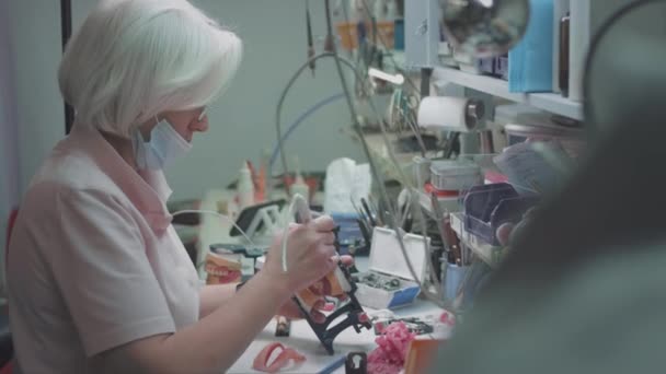 Médico femenino adulto crea una mandíbula dentaria en el laboratorio. Cirujano sosteniendo una prótesis dental. Tecnología avanzada en odontología. Producción de implantes dentales y dientes artificiales. EPIC ROJO. — Vídeo de stock