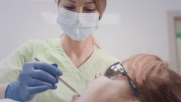 Krásná doktorka pracující s pacienty starší ženy. Doktor zkoumá zuby staré ženy v křesle. Dívka vloží lékařské nástroje do úst své babičky. — Stock video