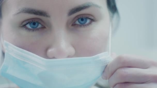 Женщина-врач надевает синюю медицинскую защитную маску. Защищает себя от вирусов во время пандемии коронавируса. Врач в больнице борется с ковидом. Близкий портрет уставшего врача. — стоковое видео