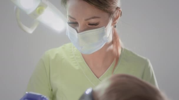 Krásná doktorka se dotýká lékařské žárovky. Pracuje s dětským pacientem. Kontroluje stav dětských zubů. Dává chlapcům do pusy lékařské nástroje. Dětská stomatologie. — Stock video