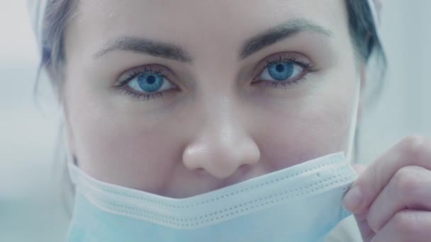 Lékařka si nasadí modrou lékařskou ochrannou masku. Chrání se před viry během pandemie koronaviru. Doktor v nemocnici bojuje s covidem. Zavřít portrét unaveného lékaře. — Stock video