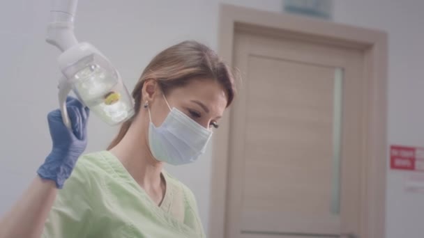 La encantadora doctora está tocando una bombilla médica. Trabaja con un paciente infantil. Comprueba el estado de los dientes de los niños. Ella pone instrumentos médicos en la boca de los chicos. Odontología infantil. — Vídeo de stock