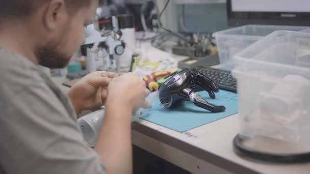 Egy robotkar protézis fekszik egy mérnöki asztalon. A szerelő megjavítja vagy létrehoz egy innovatív kéz protézist, teszteket. A kéz és a tenyér elhajlott. — Stock videók