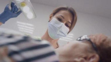 Sevimli bayan doktor yaşlı bir hastayla çalışıyor. Bir ışık lambasını hareket ettirir. Doktor sandalyedeki yaşlı kadının dişlerini muayene ediyor. Kız büyükannesinin ağzına tıbbi aletler takıyor.