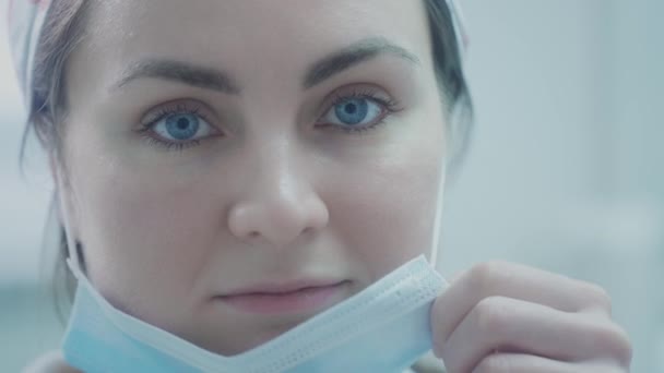 아름다운 여성 의사가 푸른 보호 마스크를 쓰고 있습니다. 코로나 바이러스가 유행하는 동안 바이러스로부터 자신을 보호 한다. 병원에 있는 의사가 필사적으로 싸우고 있어 — 비디오
