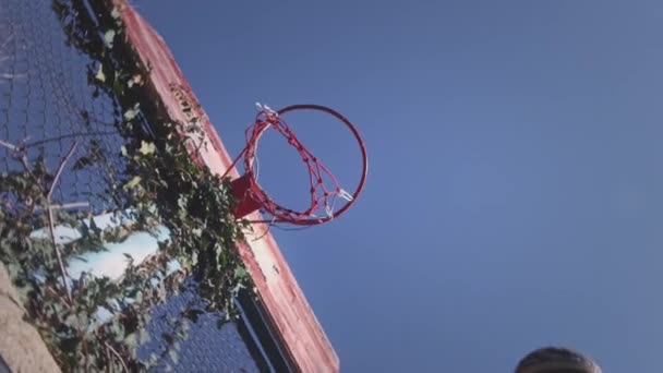 Vista hacia arriba, una pelota de baloncesto golpea la canasta en el patio de deportes. El jugador lanza con éxito la pelota en el aro, marca un punto, un gol de tres puntos. Motivación callejera y deportiva. Movimiento lento. — Vídeos de Stock