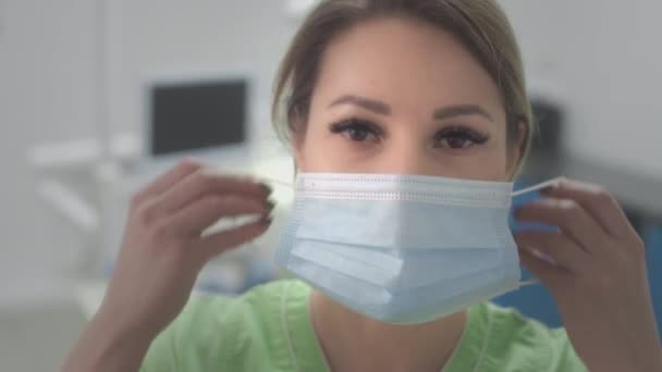 A doktornő felvesz egy kék orvosi védőmaszkot. Koronavírus-világjárvány idején megvédi magát a vírusoktól. Egy orvos a kórházban mohón küzd. Egy fáradt orvos közeli portréja. — Stock videók