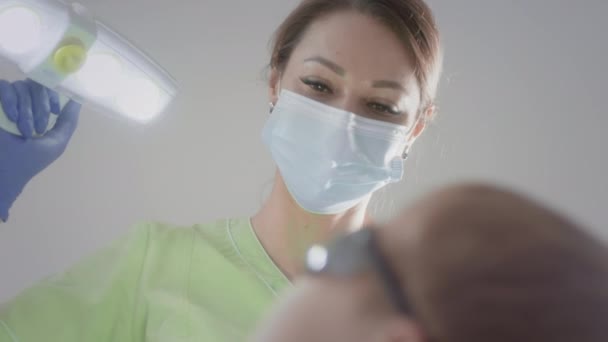 Krásná doktorka se dotýká lékařské žárovky. Pracuje s dětským pacientem. Kontroluje stav dětských zubů. Dává chlapcům do pusy lékařské nástroje. Dětská stomatologie. — Stock video