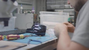 Bir robotik kol protezi mühendislik masasında yatıyor. Bir tamirci yenilikçi bir el protezi yapar ya da tamir eder, test eder. El ve avuç içi bükülmüş.