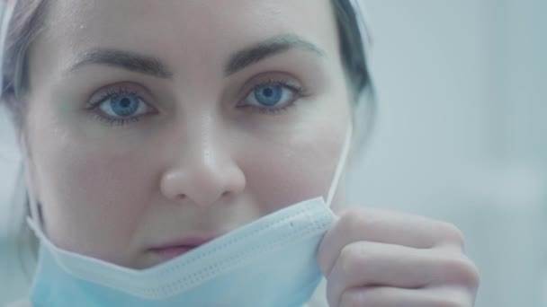 A gyönyörű doktornő kék orvosi védőmaszkot visel. Megvédi magát a vírusoktól a koronavírus világjárvány idején. Egy orvos a kórházban harcol. — Stock videók