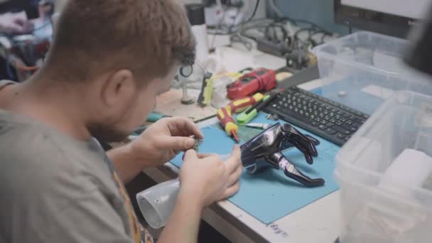 Una prótesis de brazo robótico se encuentra en una mesa de ingeniería. Un reparador repara o crea una prótesis de mano innovadora, pruebas. La mano y la palma están dobladas — Vídeo de stock