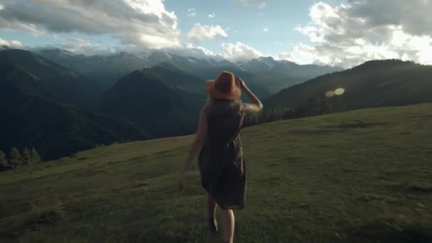 Kamera seuraa hipsterin tuhatvuotista nuorta naista pitkässä puvussa, joka kehittyy tuulessa vuoren huipulla auringonlaskun aikaan, nostaa kädet ilmaan, onnellisena ja humalassa elämästä, nuoruudesta ja onnellisuudesta. — kuvapankkivideo