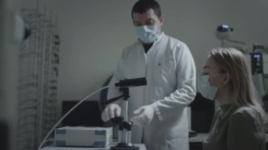 Koruyucu tıbbi maske takan bir kadın göz doktoru randevusunda gözlerini kontrol ediyor. Gözbebeğine yeşil bir lazer ışıldar. Görsel keskinliğini kontrol eden genç bir kadın - oftalmoloji tedavisi