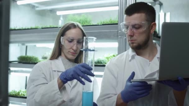 Mujeres y hombres científicos en el laboratorio. Examine el líquido azul en un tubo de ensayo. La investigación se realiza, los datos se introducen en la base de datos. Concepto: investigación, bioquímica, medicina farmacéutica — Vídeo de stock