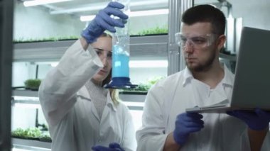 Laboratuvardaki kadın ve erkek bilim adamları. Mavi sıvıyı test tüpünde inceleyin. Araştırma yapılıyor, veri veritabanına giriliyor. Konsept: araştırma, biyokimya, ilaç