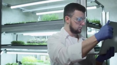 Erkek bilim adamı laboratuvarda çalışmak için bir dizüstü bilgisayar kullanır. Biyolojik verileri analiz eder. Bitkiler üzerinde biyokimya ile araştırma yapıyor. Bilimsel botanik araştırması. Büyüyen Mikroçimler