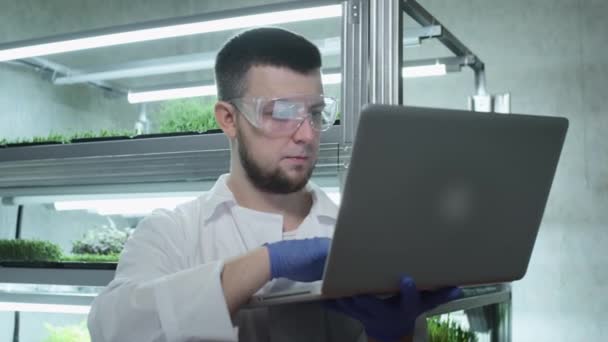 Mužský vědec používá notebook k práci v laboratoři. Analyzuje biologická data. Provádějí výzkum s biochemií rostlin. Vědecký botanický výzkum. Pěstování mikrozeleně — Stock video