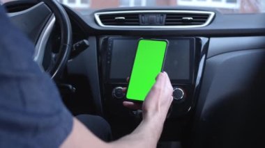 Erkek bir sürücü, elinde telefonu tutan yeşil ekranlı akıllı telefonu dikey olarak kullanır. Navigator ya da yol başvurusu için bir model. Parmağınızla sağa ya da sola kaydırın. Fotoğraflar arasında kaydırmalar.