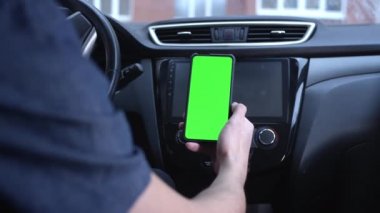 Erkek bir sürücü, elinde telefon tutan yeşil ekranlı akıllı telefonu dikey olarak kullanır. Navigator ya da yol başvurusu için bir model. Uzaklaşır, haritayı kaldırır. Şehir haritasında bir rota oluştur