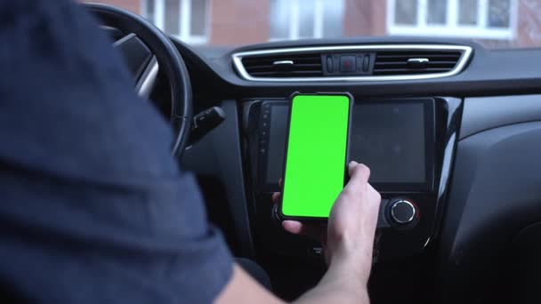 Un conductor masculino utiliza un teléfono inteligente verticalmente con una pantalla verde, sostiene un teléfono en su mano. Mockup para un navegador o aplicación en carretera. Acércate, examina la tarjeta. Construir una ruta en un mapa de la ciudad — Vídeos de Stock