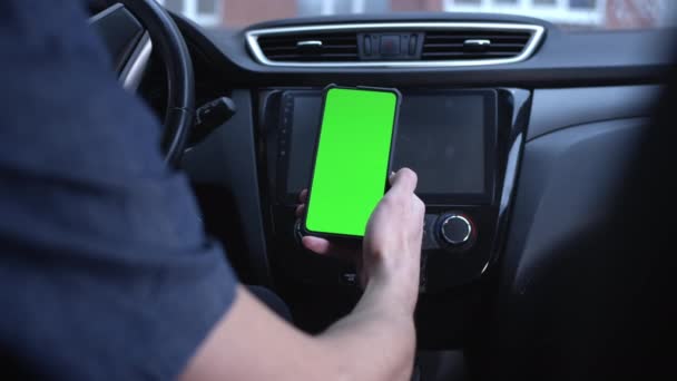 Un conductor masculino utiliza un teléfono inteligente verticalmente con una pantalla verde, sostiene un teléfono en su mano. Mockup para un navegador o aplicación en carretera. Desliza hacia arriba y hacia abajo. Aplicación de citas. — Vídeos de Stock