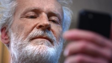Yaşlı adam elinde bir akıllı telefon tutuyor ve onu kullanıyor. Büyükbabam sosyal ağlara bakıyor ve cihaza bir mesaj yazıyor. Çocuklara video görüşmesi yap ya da internetten yemek sipariş et..