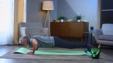 Gri saçlı yaşlı bir adamın portresi, şınav, egzersiz. Arka ve kolların eklemleriyle ev yapımı spor hareketleri. Büyükbabam mükemmel bir atletik vücut şekline sahip. Spor giyimli yaşlı adam.