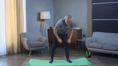Gri saçlı, sakallı yaşlı bir adamın portresi öne eğiliyor. Evde tendonları ve bacak kaslarını germek için egzersiz yapıyor. Büyükbaba bayırları yapıyor, yere kadar uzanıyor.
