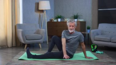 Gri saçlı, sakallı, sırtüstü uzanan yaşlı bir adamın portresi. Oturma odasında, kaburgalar arasındaki egzersizler, interkostal nöroloji. Spor giyimli yaşlı adam..