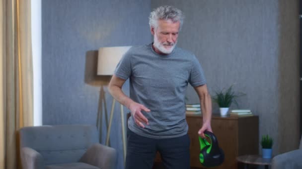 Šedovlasý starší muž s plnovousem cvičí s kettlebellem. Dědeček v obýváku zvedá váhu. Stařík ve sportovním oblečení. Úspěch a úspěch po tvrdé práci. — Stock video